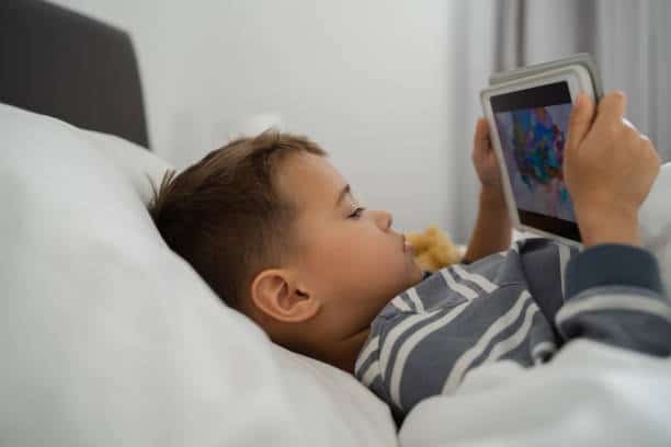 Toddler Boy Engrossed in Tablet Technology in Bed.